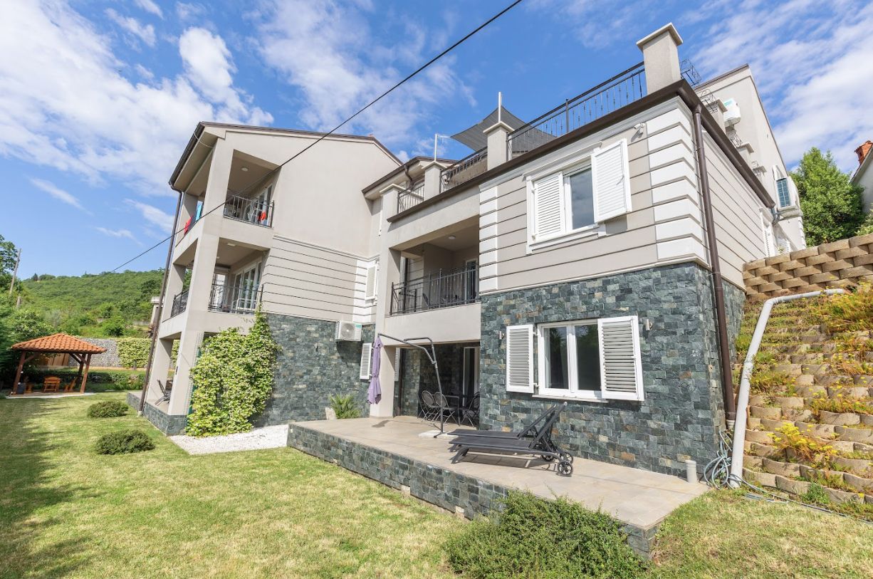 The house: grey stone facade, lawn and terraces
